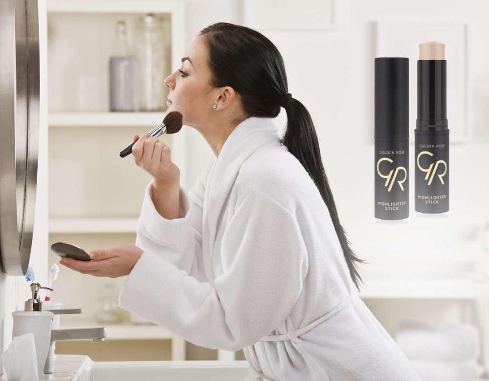 A young woman is putting on makeup in front of a mirror. She is looking away from the camera. Horizontally framed shot.