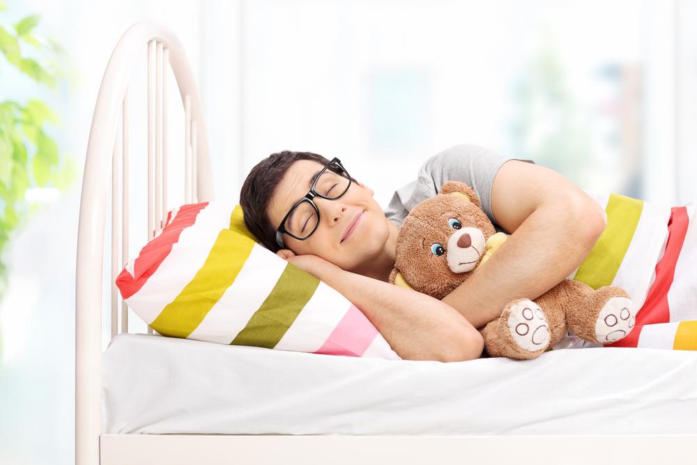 Childish young man sleeping with a teddy bear