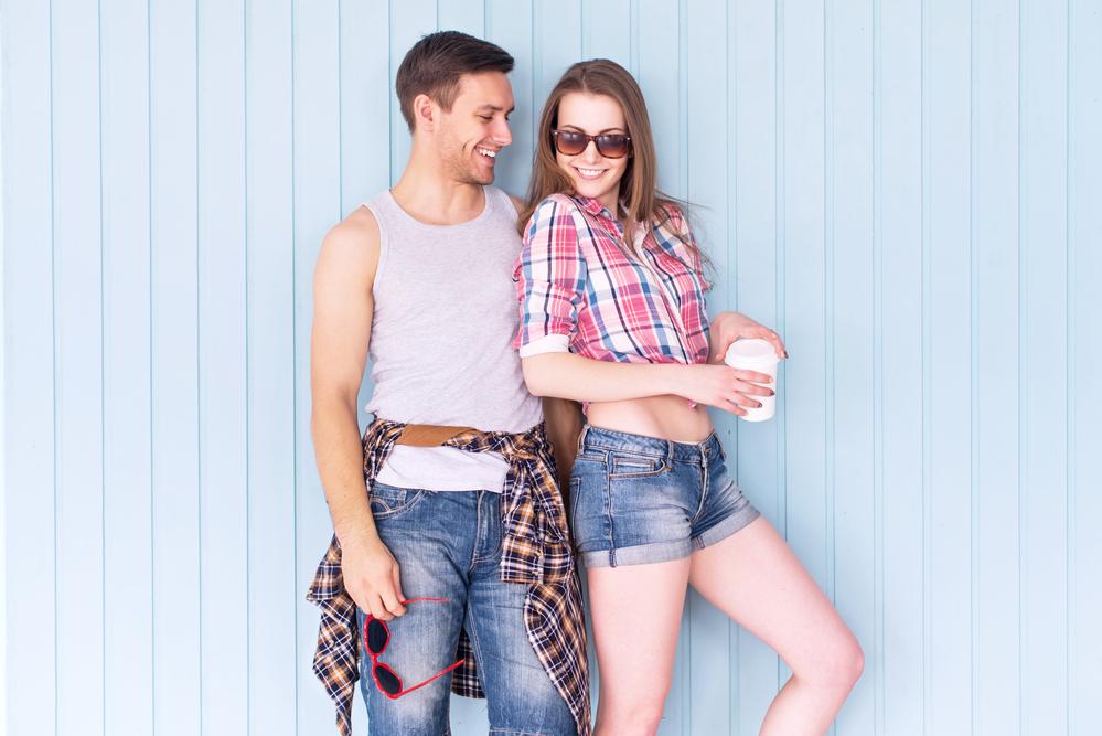 Happy couple friends wearing sunglasses in summer jeanswear street urban casual style talking having fun standing near wall