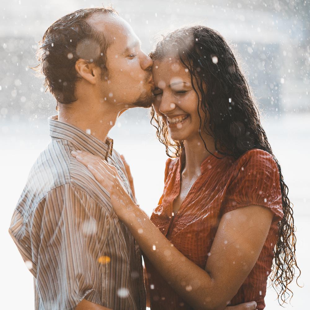 cople in love hugging and kissing under summer rain