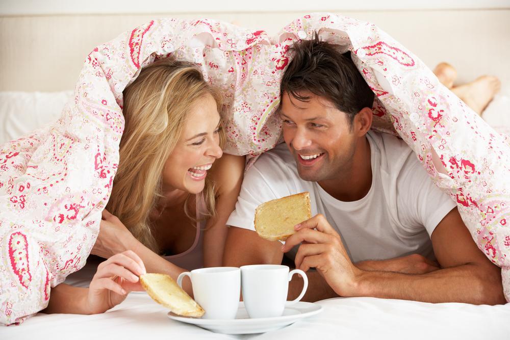 Couple Snuggled Under Duvet Eating Breakfast