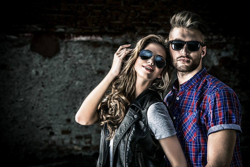 Couple of young people in jeans clothes posing outdoors over brick wall.