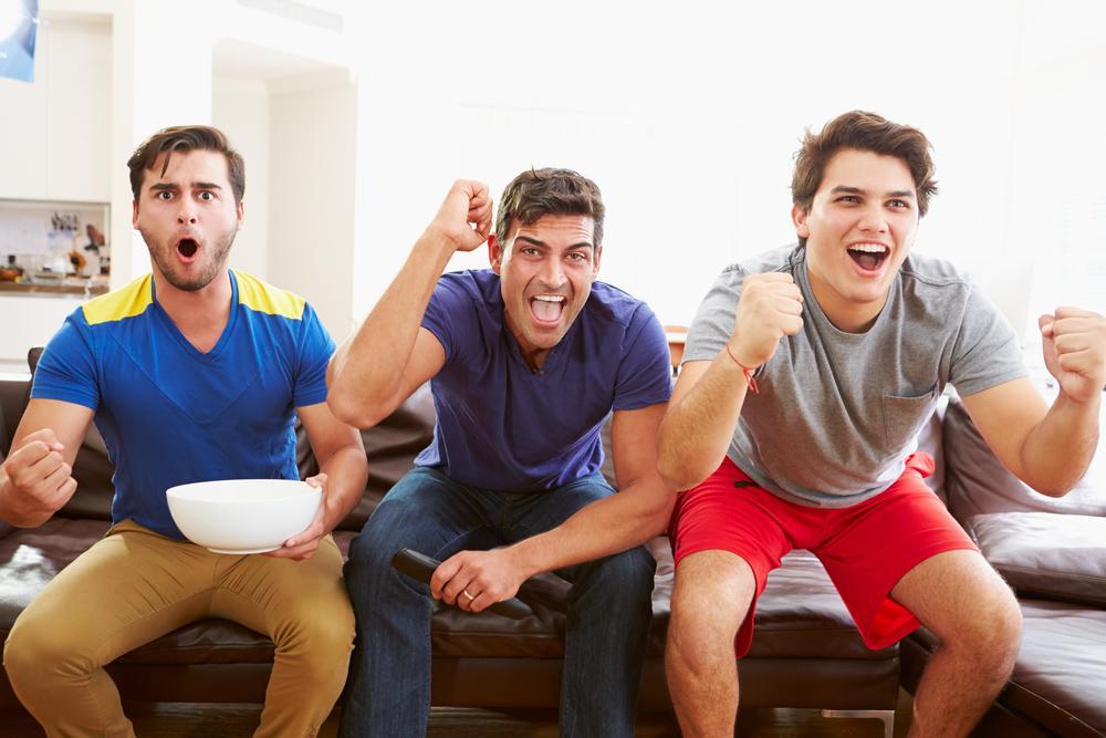 Group Of Men Sitting On Sofa Watching Sport Together