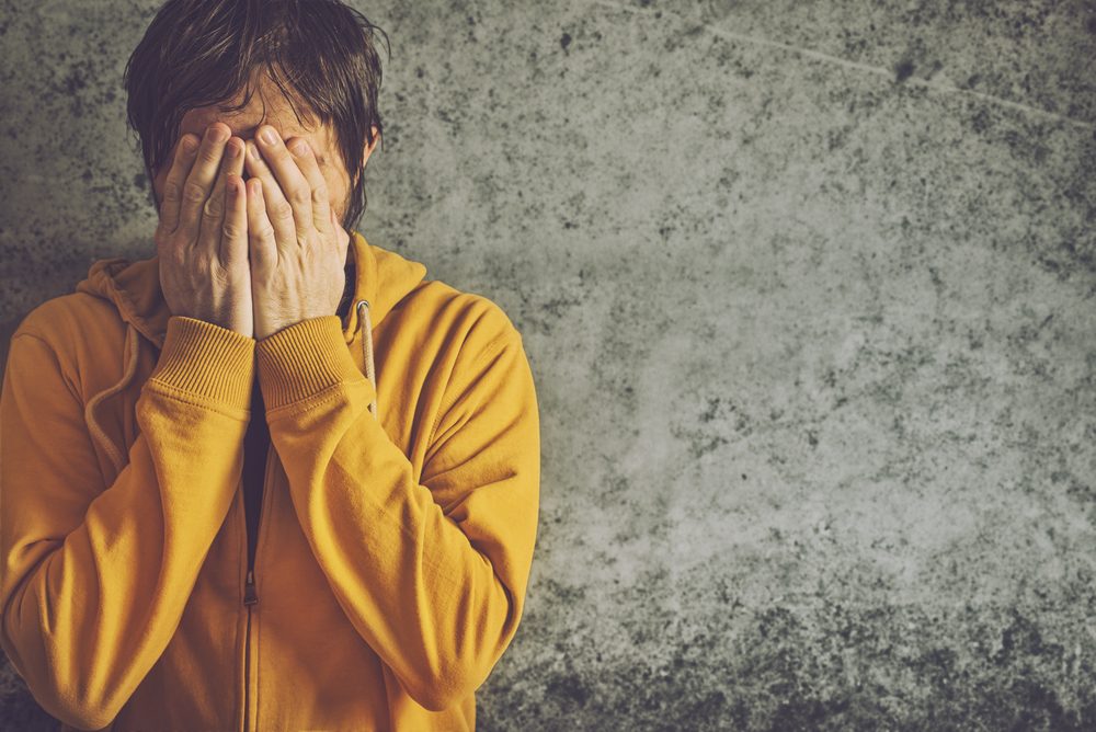 Upset Depressive Adult Man Wearing Yellow Jacket is Crying with his Face Covered.