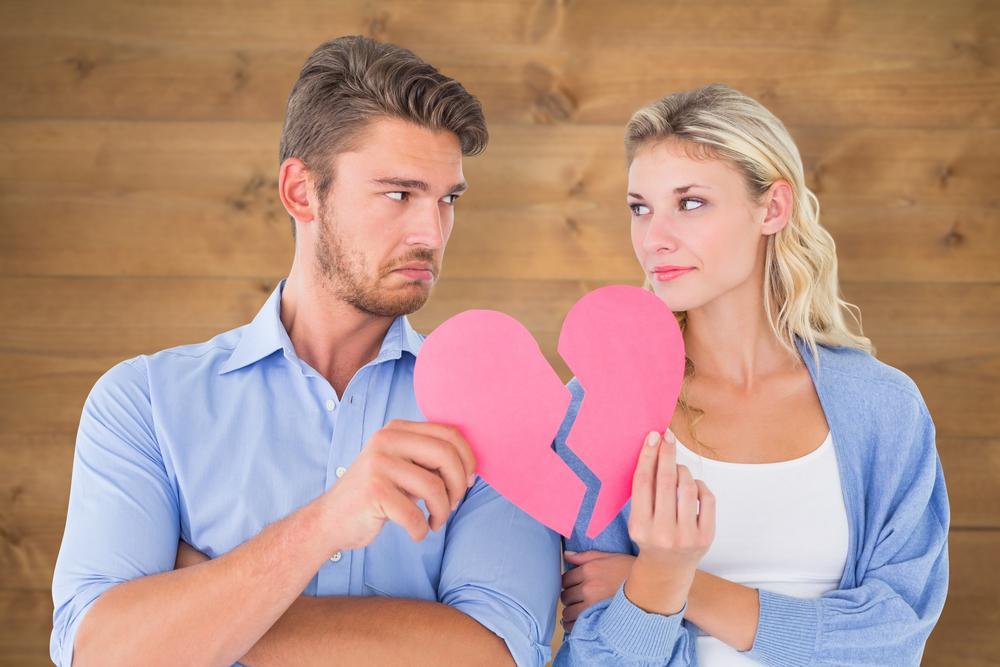 Couple holding two halves of broken heart against bleached wooden planks background