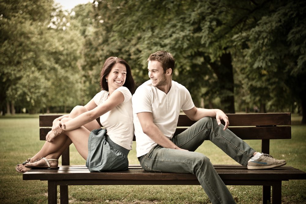 Young smiling couple looking on each other - sitting on bench