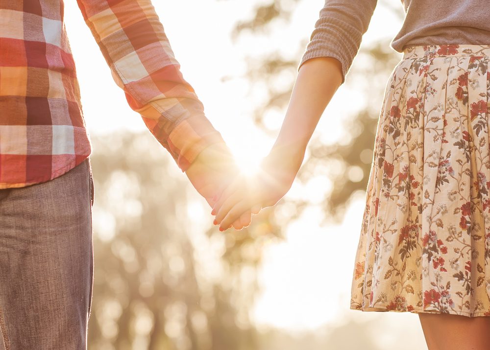 Young couple in love walking in the autumn park holding hands looking in the sunset