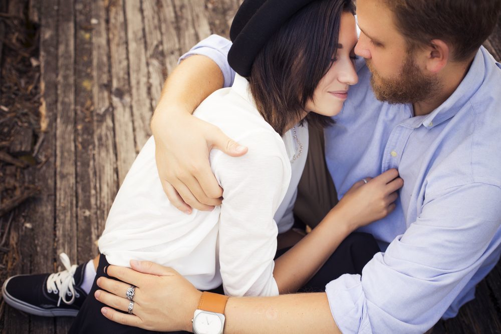 Beautiful hipster couple in love on a date outdoors in park having fun. Bearded redhair man. Brunette woman in black skirt and white blouse and black hat