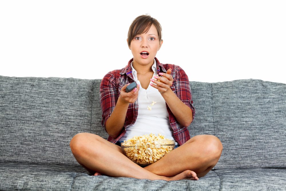 Young woman eating popcorn while watching tv isolated on white background