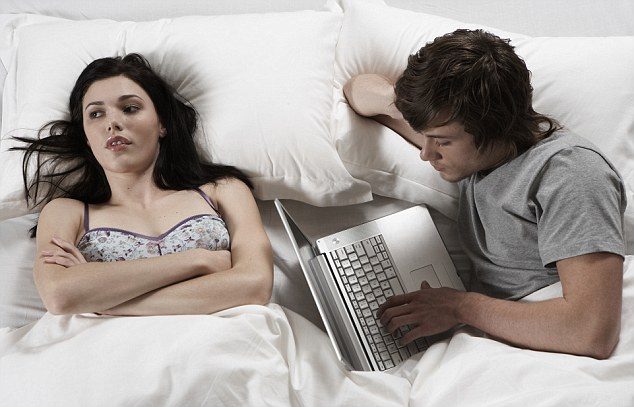 Young man and woman lying in bed, man using laptop, overhead view