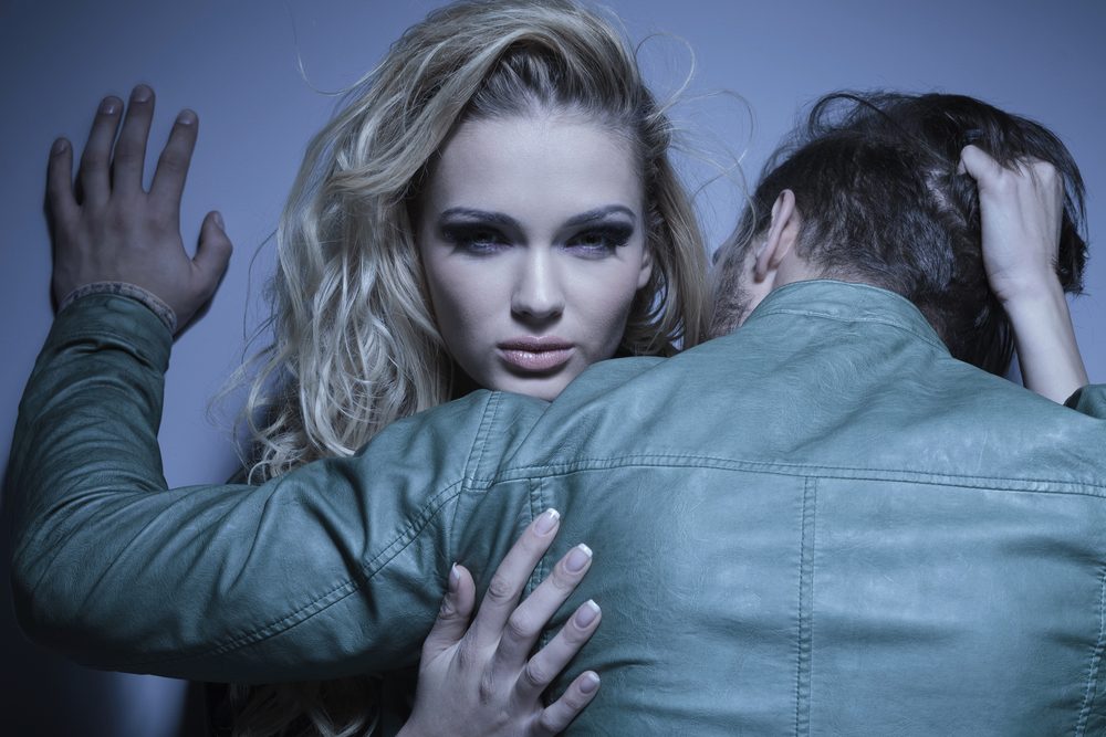 young woman is pulling her boyfriend to her by his hair, man standing with his back at the camera while embracing his lover