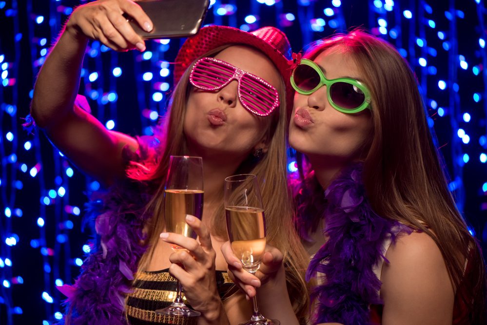 Two beautiful young women with glasses of champagne making selfie at party in night club