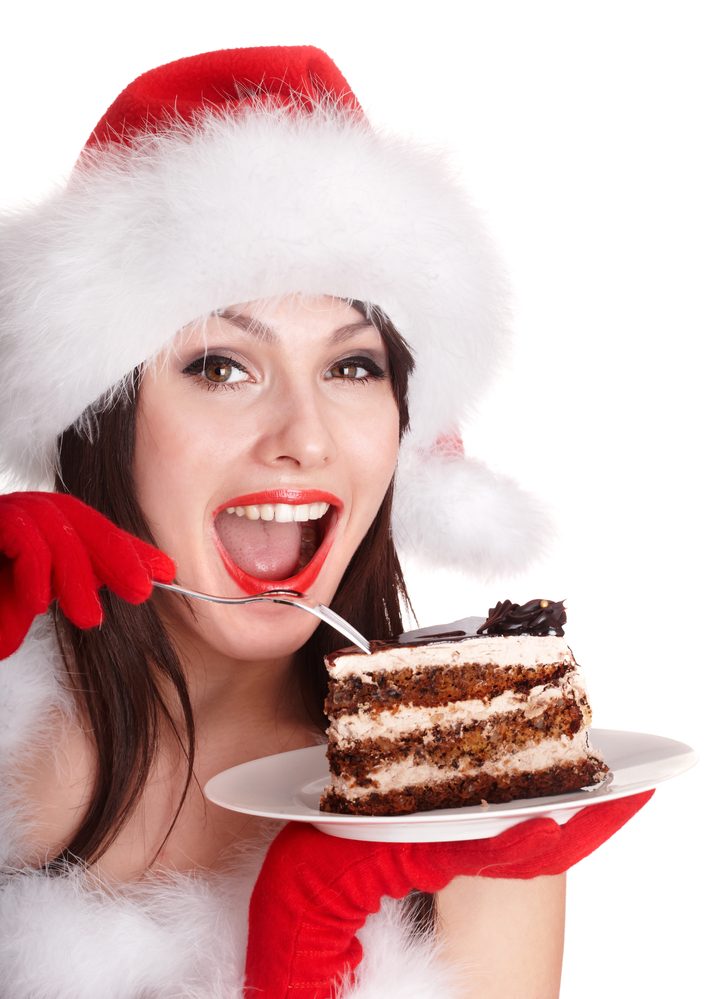 Christmas girl in red santa hat eating cake on plate. Isolated.