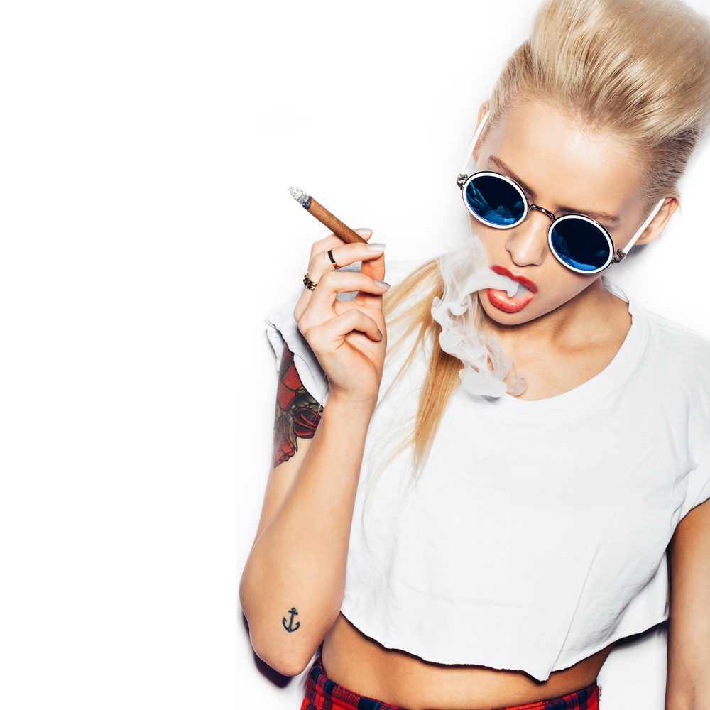 Sexy woman in sunglasses and white t-shirt blowing smoke from a cigar. Swag style girl. White background, not isolated