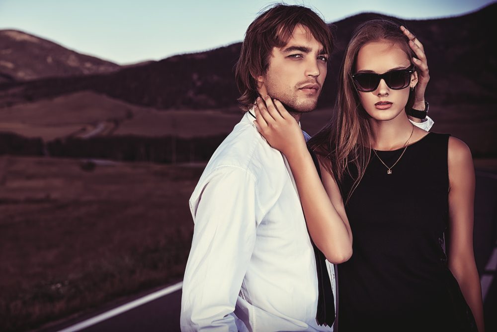 Passionate couple of young people posing on a road over picturesque landscape.