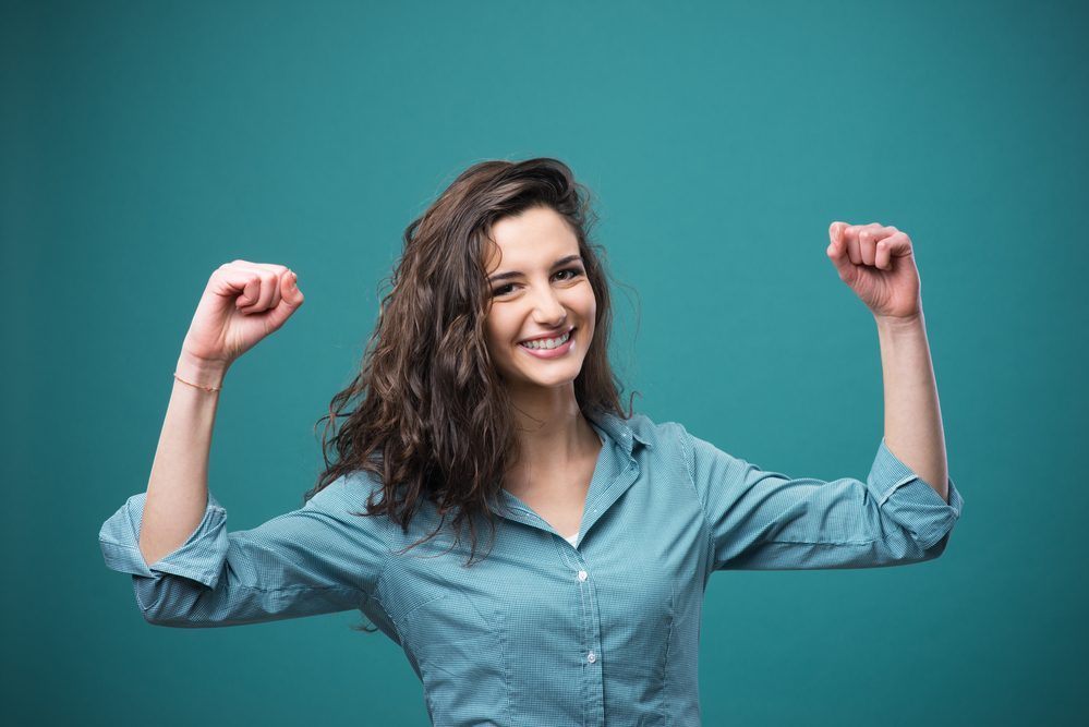 Cheerful young woman smiling with raised fists