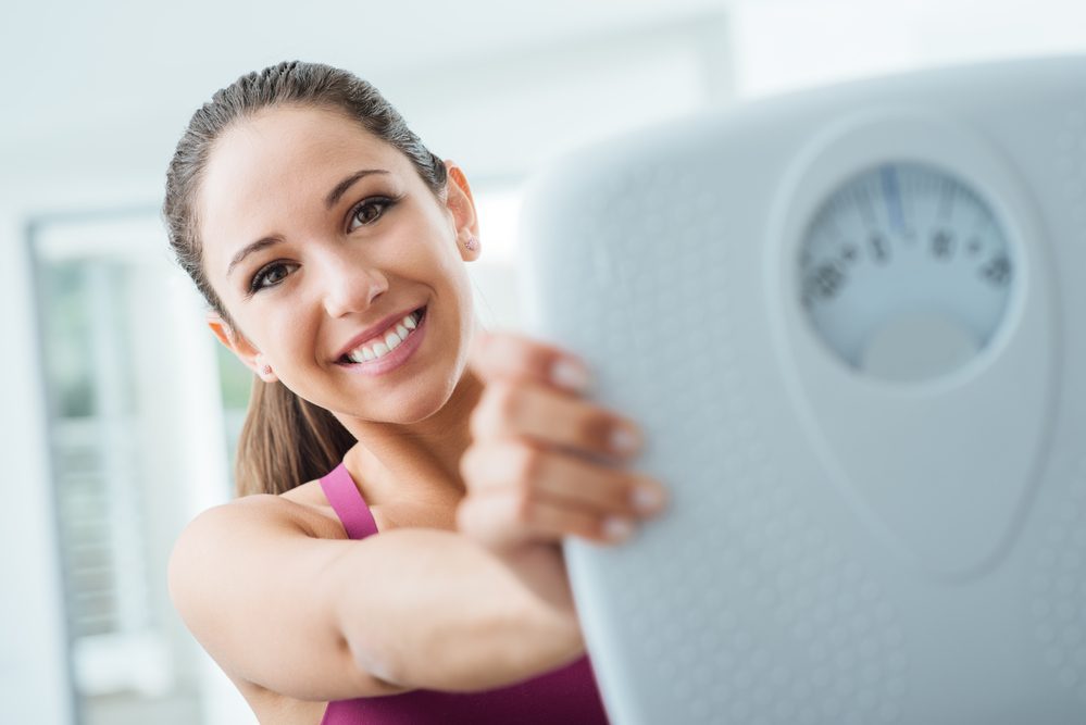 Happy young woman losing weight and showing a scale, dieting and fitness concept