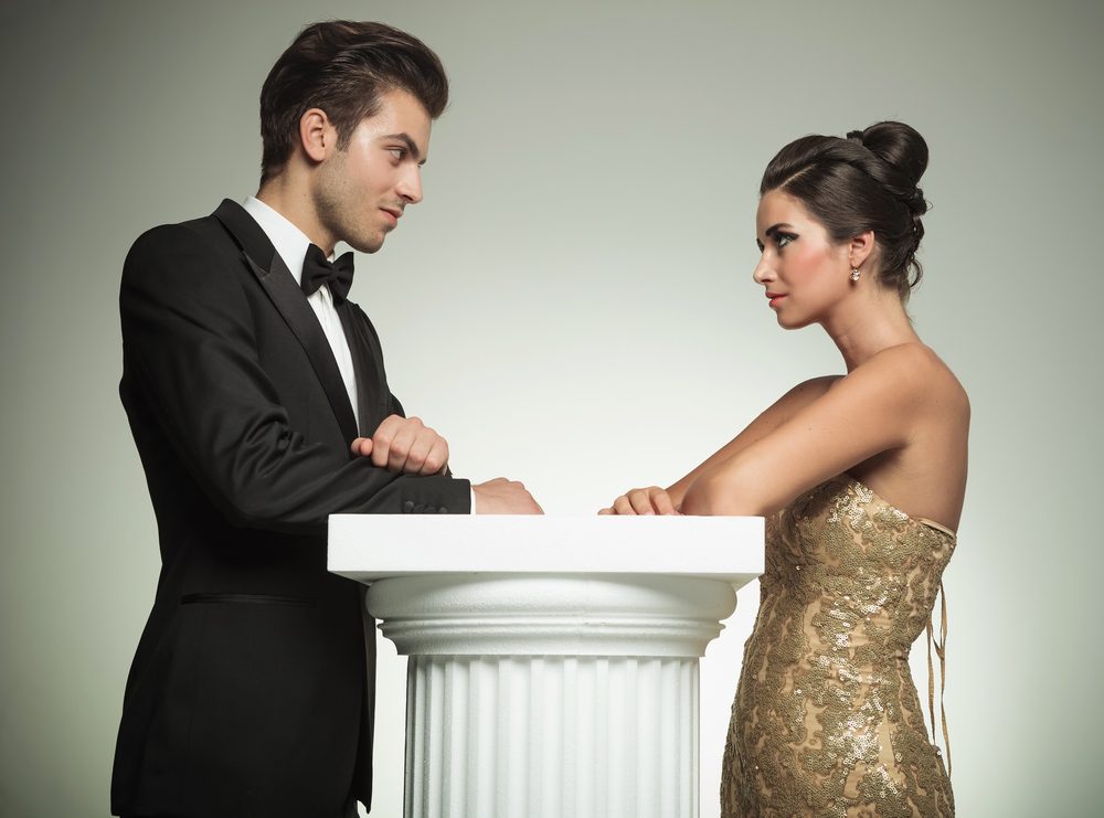 happy man and woman in evening clothes lean on a column and look at each other in studio