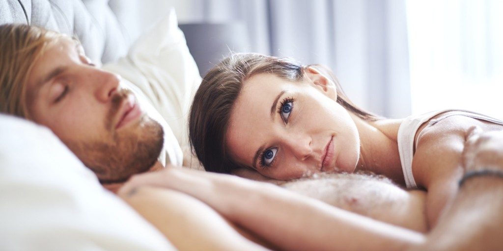 Pensive woman laying on sleeping man on bed