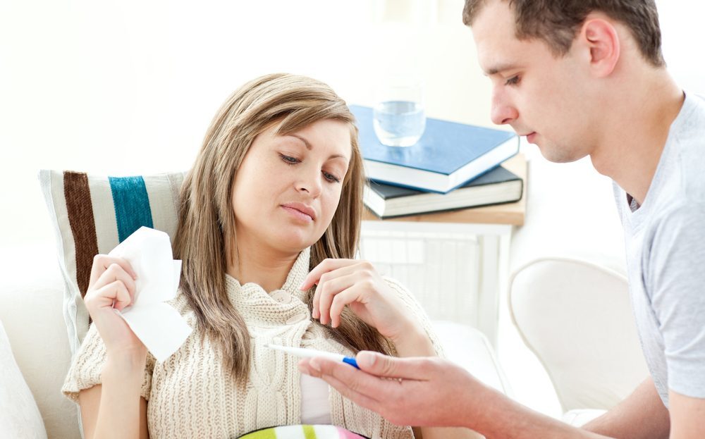 Beautiful sick woman getting pills from her boyfriend lying on a sofa