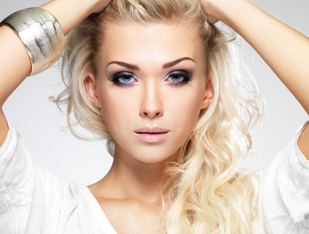 Fashion model posing in studio. Portrait of a beautiful blond woman with saturated makeup. Girl posing on white background