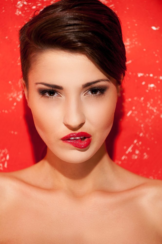 Beauty and passion. Portrait of beautiful young shirtless woman standing against red background and biting lips