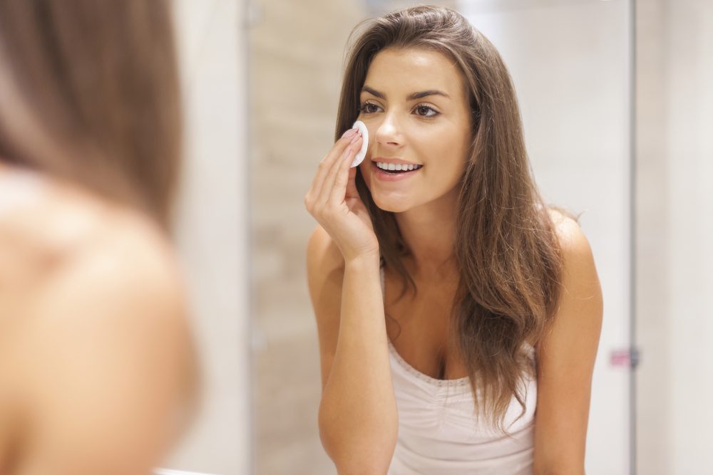 Beautiful brunette woman removing makeup from her face