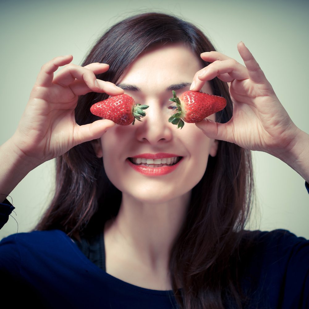 beautiful woman with strawberries on eyes on gray background