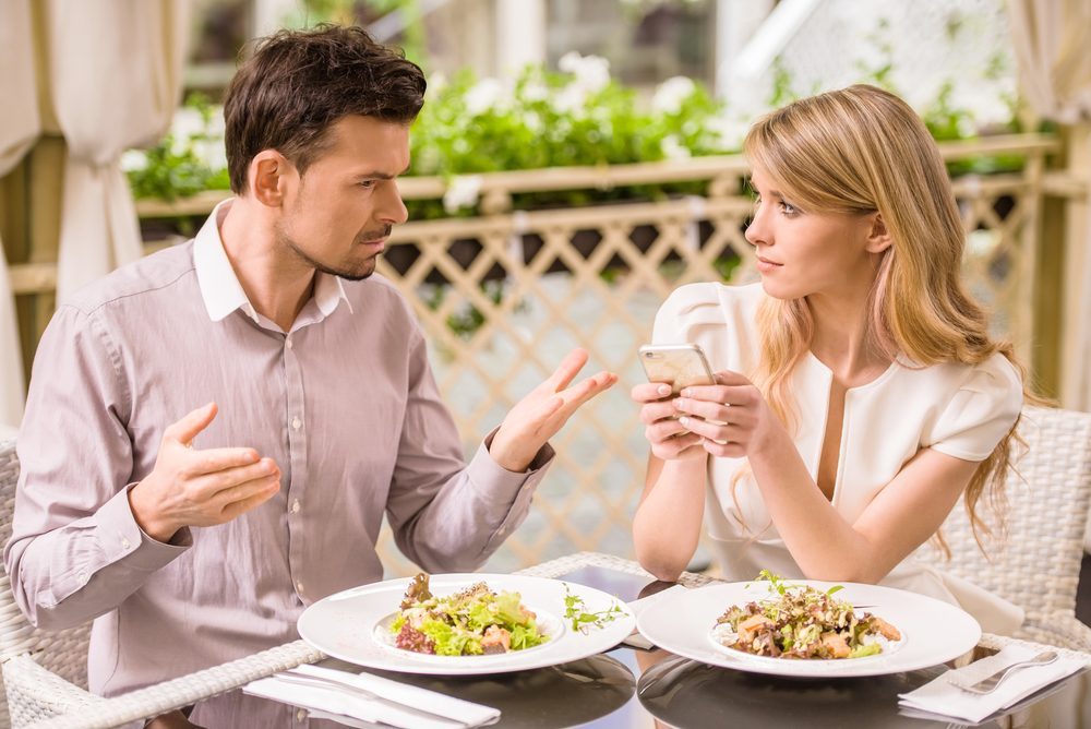 Man is getting nervous in restaurant while his woman looking at phone.