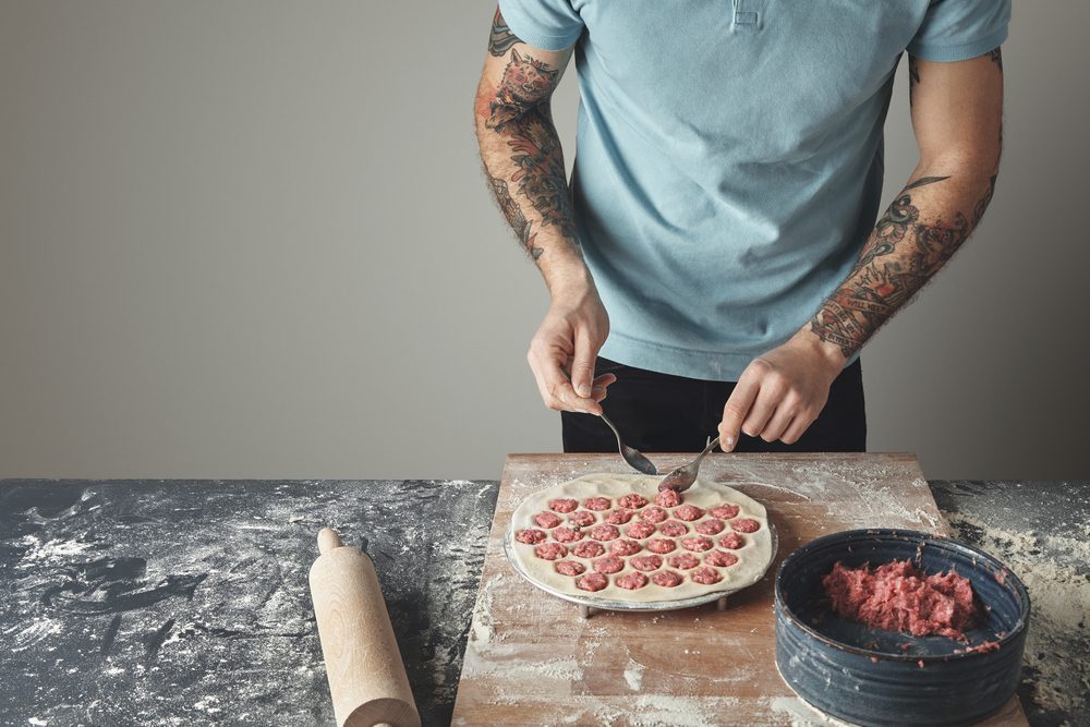 Tattooed chief man cooks pelmeni or dumplings or ravioli in spec