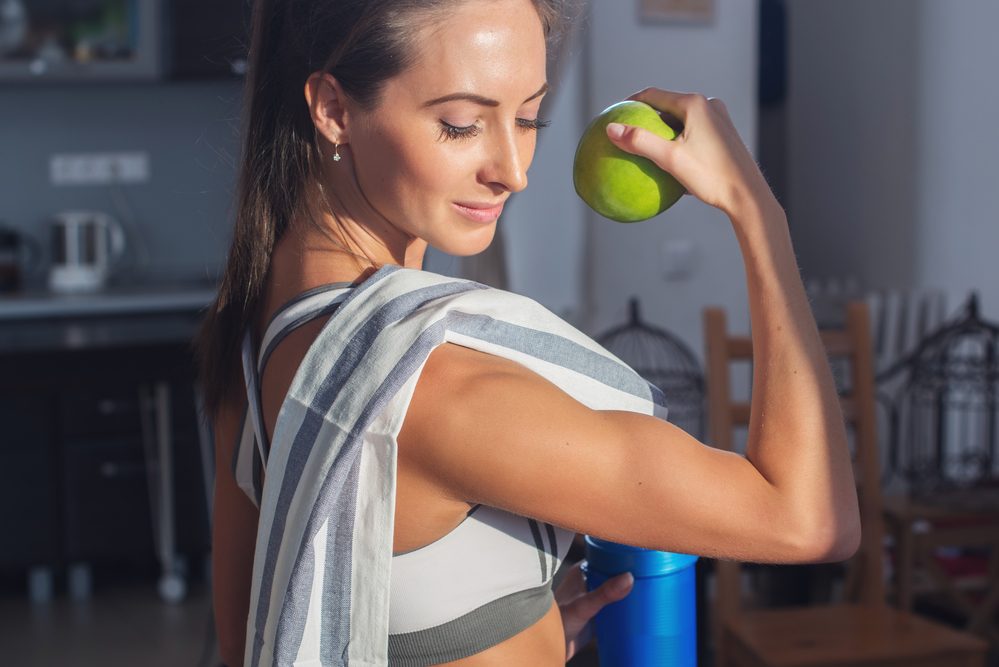 Active athletic sportive woman with towel in sport outfit holding apple showing biceps healthy lifestyle.