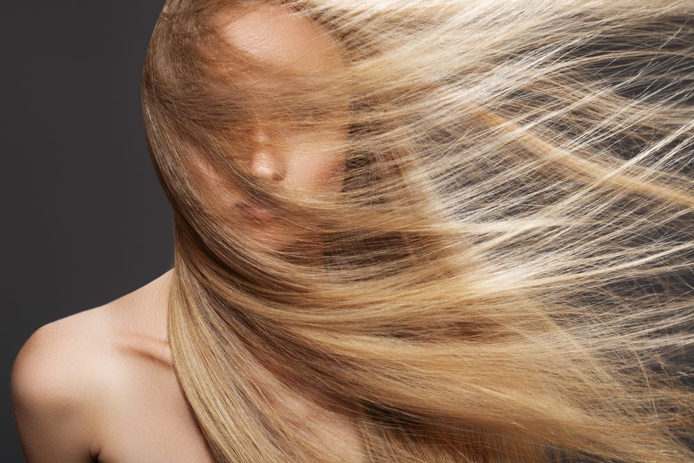 Wellness and spa. Sensual woman model with windswept flying dark blond hair on gray background.