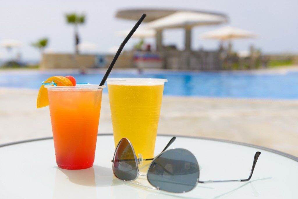 Refreshing summer cocktails and a pair of sunglasses on a table beside a swimming pool at a vacation resort.