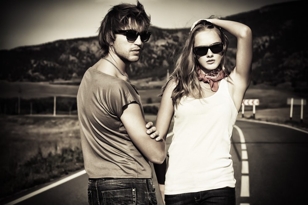 Couple of modern young people posing on a road over picturesque landscape.