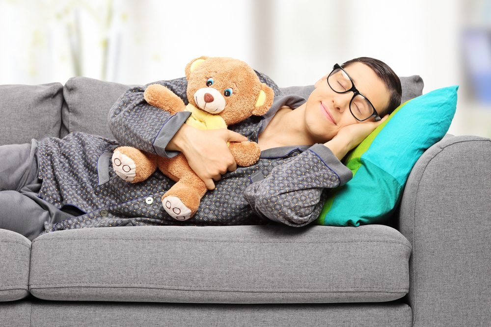 Young man holding teddy bear and taking a nap on couch, at home