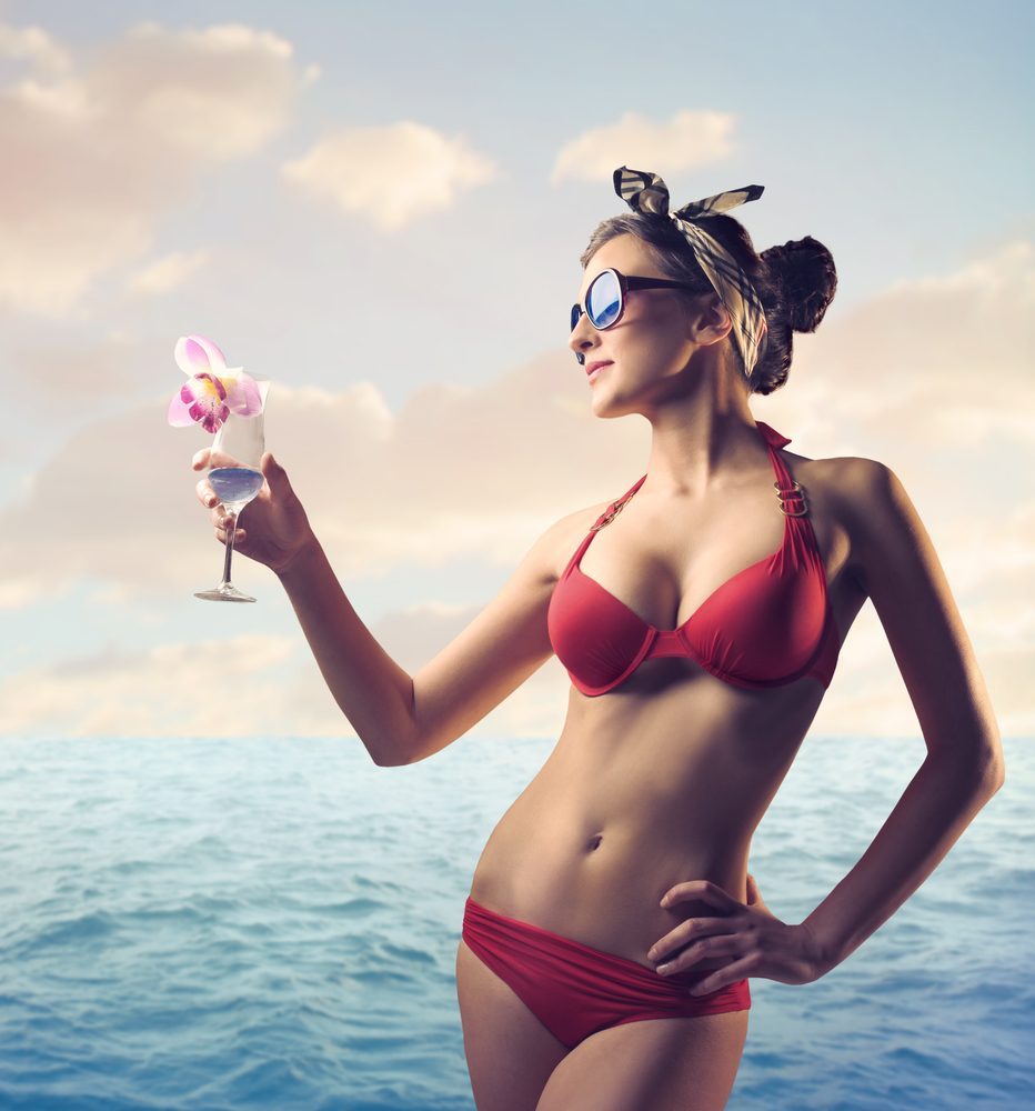 Beautiful woman in bathing suit holding a cocktail at the seaside