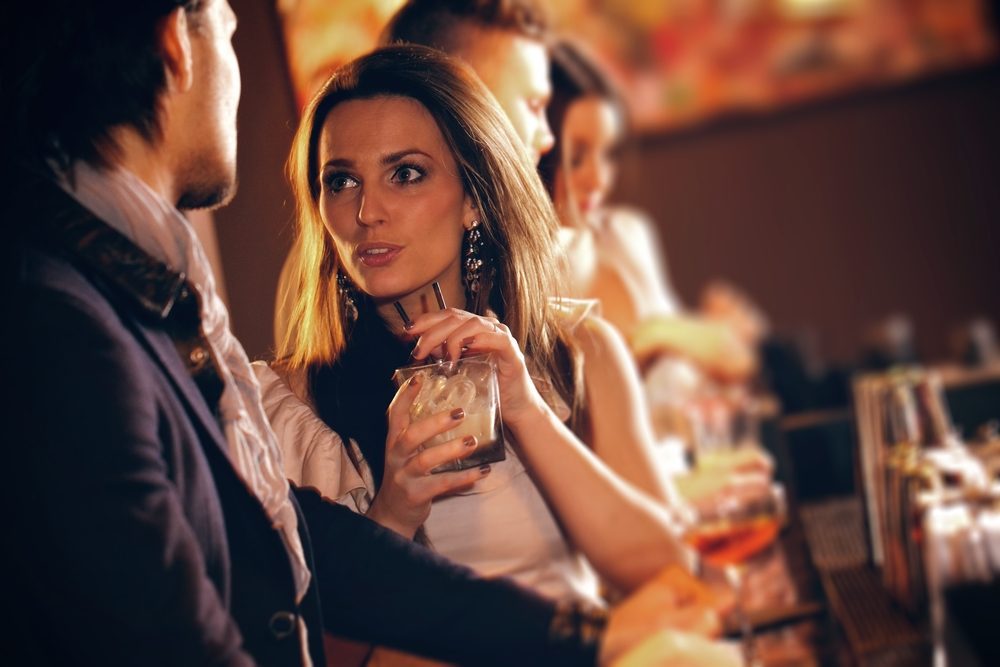 Young woman with a glass of wine talking to a man at the bar