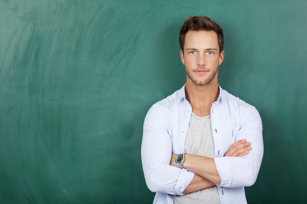 Portrait of a serious young man standing against green chalkboard