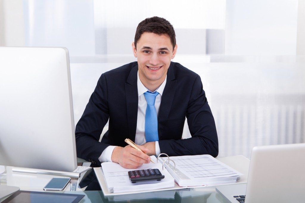 Portrait of smiling businessman calculating tax at desk in office