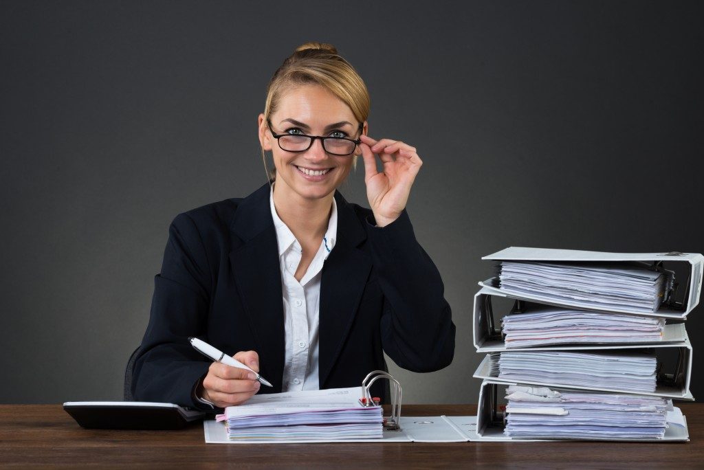 Portrait of smiling young businesswoman wearing eyeglasses while writing on document at desk