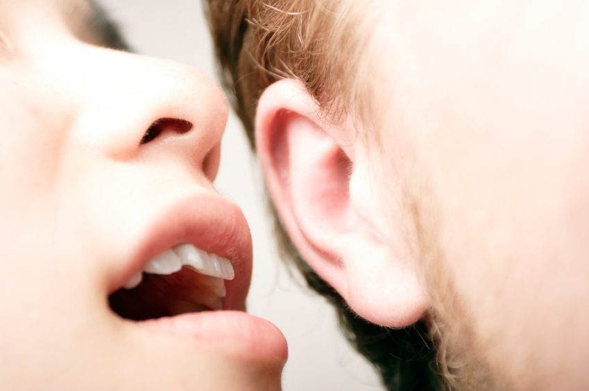 Girl whispering into guy's ear.