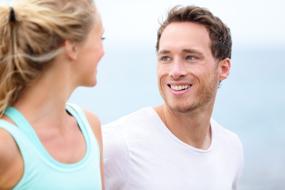 Couple jogging training together running on beach living healthy lifestyle. Man runner smiling at woman during workout. Closeup of handsome male fitness model outside.