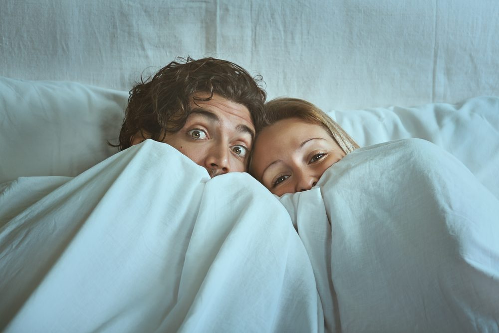 Frightened couple with eyes wide open under the sheets. Fear and shock concept