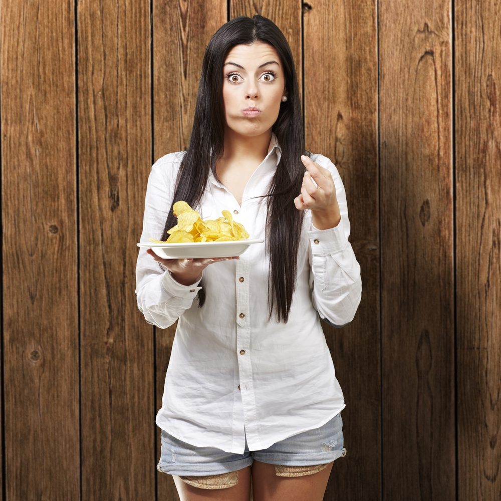young woman eating potatoe chips against a wooden background
