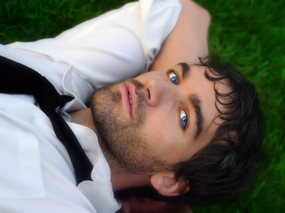 Close-up portrait of young good looking man in white shirt against grass