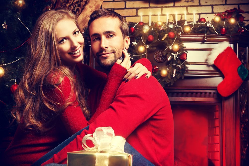 Happy young people give each other gifts by the fireplace near the Christmas tree.